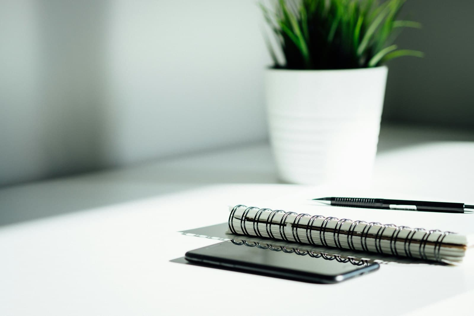 Notebook, pen and phone on a bright white desk